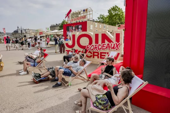 des visiteurs de Bordeaux Fête le Vin s'attardent sur des transats devant le stand rouge de la campagne Join the Bordeaux Crew